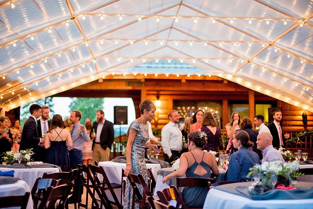 Guests mingle and converse at an outdoor event under a transparent tent with string lights at our charming inn in Pagosa Springs, surrounded by decorated tables and a festive atmosphere.